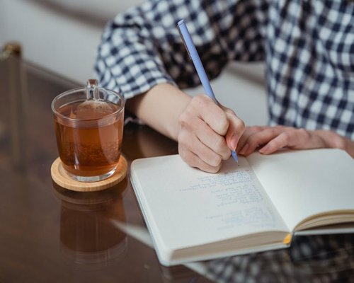Person writing in a daily habit journal while drinking tea